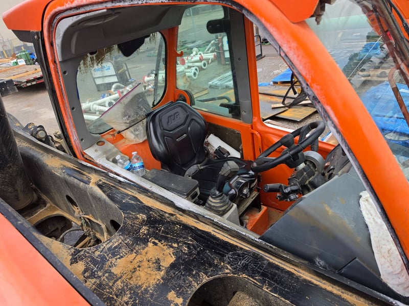 Front cab glass removed from an orange rough-terrain telehandler at an industrial yard