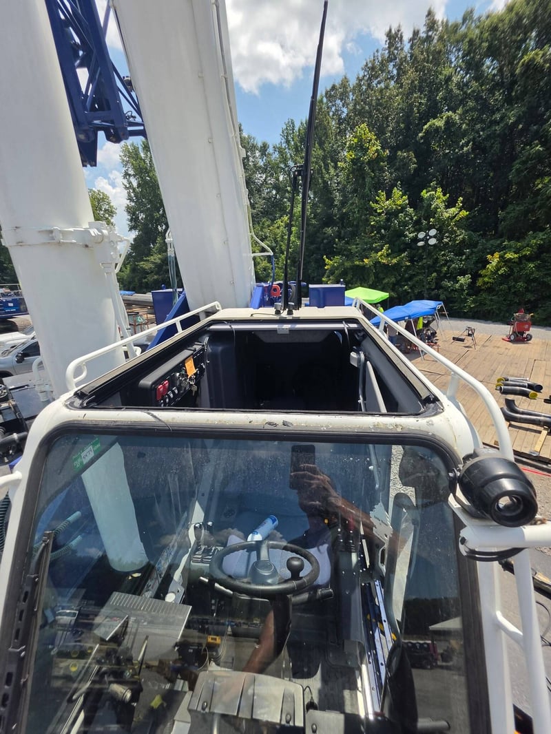 Operator cab of a white boom crane with the front glass removed, viewed from below